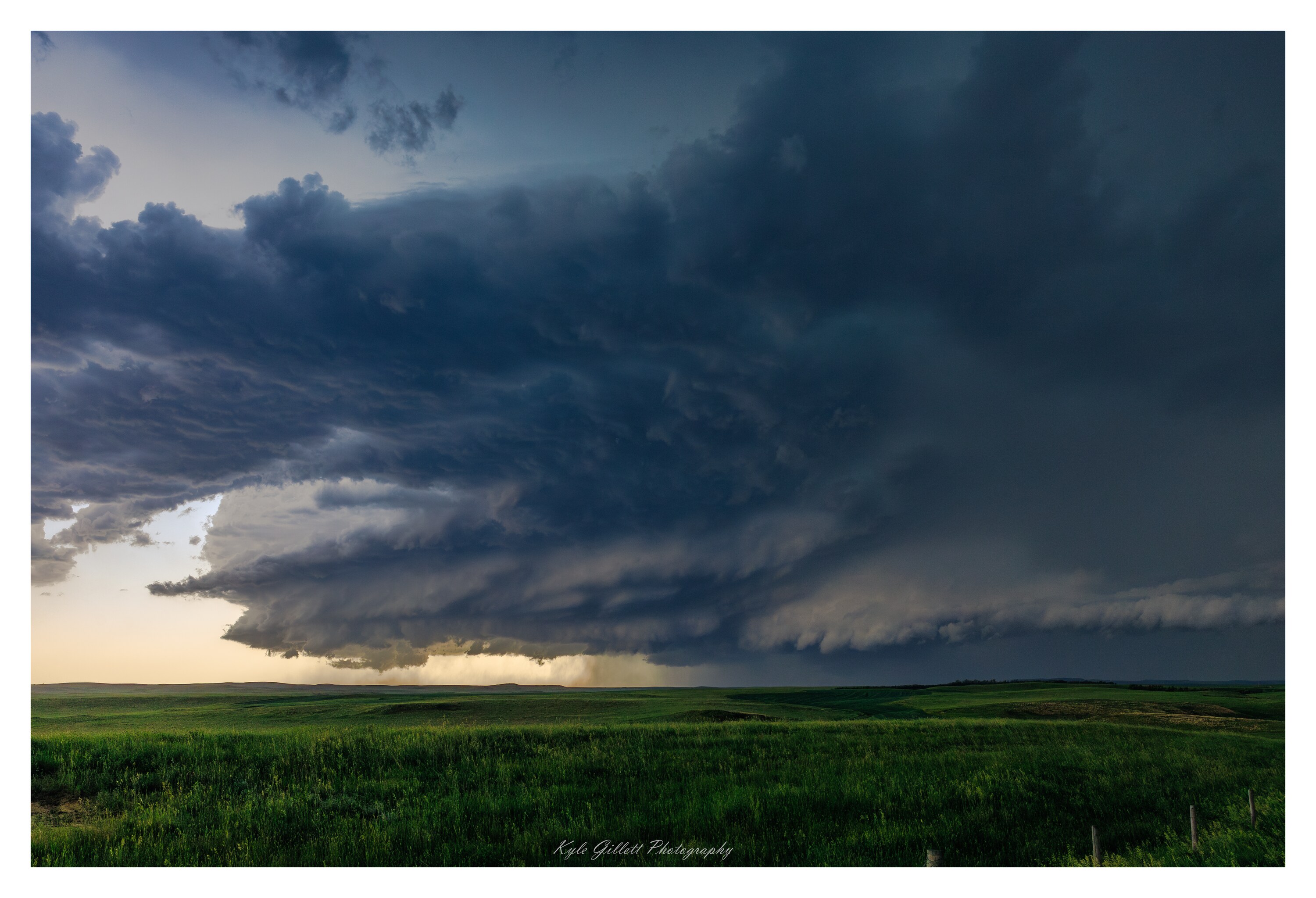 A broad supercell storm structure over green plains at sunset.