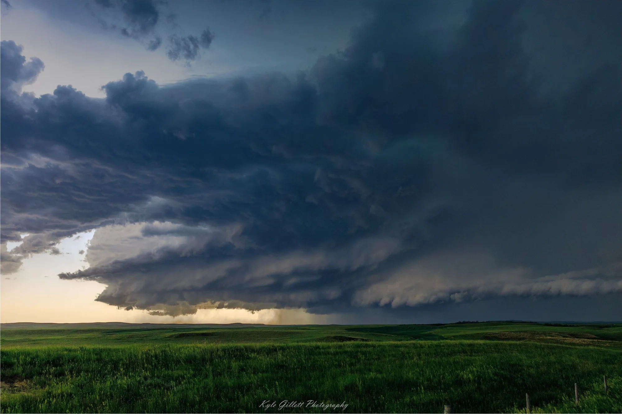 A broad supercell storm structure over green plains at sunset.